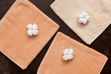 Terry beige towels and cotton flowers on a dark brown rustic background. The concept of natural fabric. Top view, flat lay.