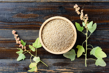 Organic brown quinoa seed in a wooden bowl and quinoa plant on wooden background, healthy food, top view