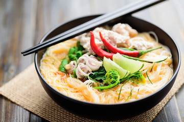 Spicy rice noodles soup with spices and herbs (Thai Tom Yum) in a bowl with chopsticks, Asian food