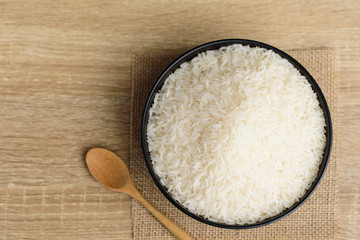 Organic Thai Jasmine rice grain in a bowl with spoon on wooden background, Top view