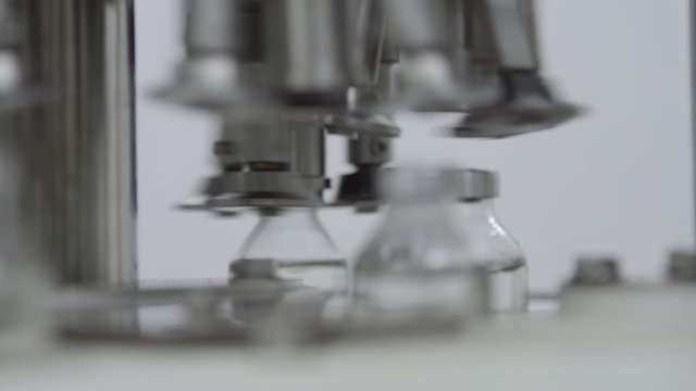 glass bottles filled and sealed with rubber caps on a medical solution conveyor line aluminium cap packaging section close up selective focus medical industry