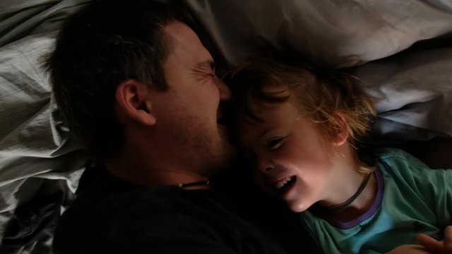 Close-up portrait of two people adult father and cute little son lying on bed at home and smiling. Paternal love, parenthood and happy family concept