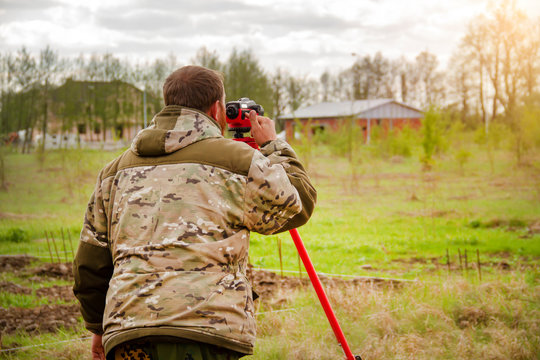 Surveyor conducts a topographic survey for cadastral work at a construction site on a background of forest and sky with clouds