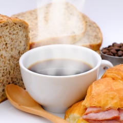 A Black coffee cup The white smoke evaporates and dark brown coffee bean roasted, french homemade Croissant, and sliced ​​cereal bread with a wooden teaspoon. Yummy and healthy concept.
