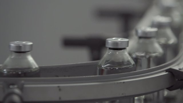 glass bottles filled and sealed with rubber and aluminum caps on medical solution conveyor line close up medical industry