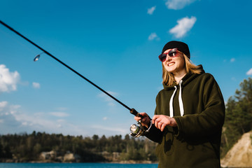 Fisherman with rod, spinning reel on river bank. Sunrise. Fishing for pike, perch, carp. The concept of rural getaway. Woman catching fish, pulling rod while fishing from lake or pond with text space.