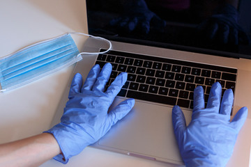 mani con guanti in lattice scrivono su computer portatile m isolato su sfondo bianco con un amascherina celeste