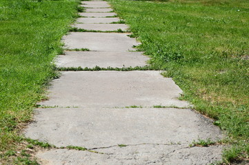 Fototapeta na wymiar Gray concrete pathway without fence in green grass
