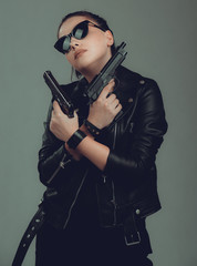 Shot of a sexy military woman posing with guns,in a black jacket,black glasses in the eyes,