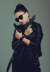Shot of a sexy military woman posing with guns,in a black jacket,black glasses in the eyes,