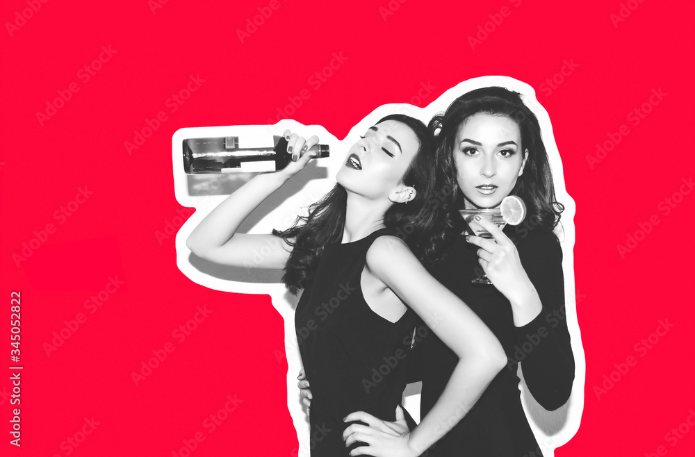 Wall mural  Two beautiful models of a girl in a black night dress hug, laugh and have fun. Twin brunettes with long hair drink an alcoholic cocktail and wine. Wine bottles cocktail isolated red background.