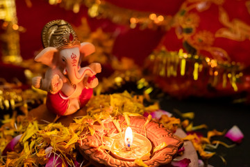 high angle shot of lord ganesha statue with terracotta lamp on rose petals against blurred background. religion concept.