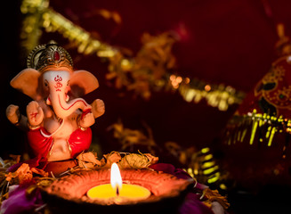 low light photography of small ganesha statue and earthen lamp on flower petals against blurry...
