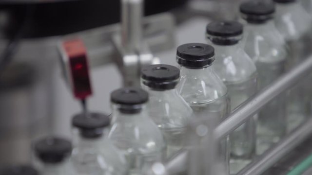 glass bottles filled and sealed with rubber caps on a medical solution conveyor line close up selective focus medical industry