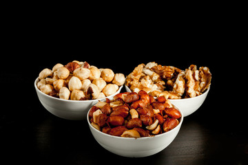 Three white ceramic bowls with hazelnuts , walnuts  and peanuts