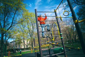 A boy in a red jacket is engaged in a sports field in the Park in the spring, climbing up the stairs. Swedish wall. Trips, sports classes for children, physical education, games in the fresh air.