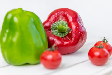 Sweet red and green peppers and cherry tomatoes on a white wooden table. Vitamins and a healthy lifestyle.