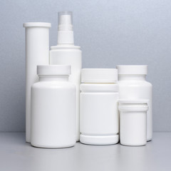 5 white vials without labels for medicines, vitamins, sprays, liquids are on a gray shelf. mockup for pharmacy and store design