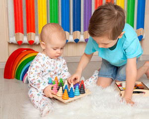 Older brother plays with younger sister in Montessori toys in the children's room. He helps the...