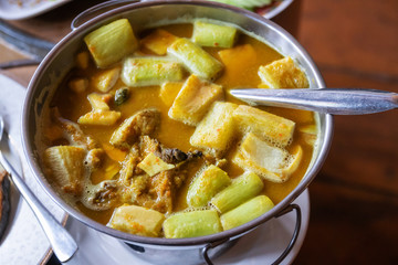 Yellow curry with fish and green taro (aaw dip) in hot pot on wooden table. Southern delicious food of Thailand.