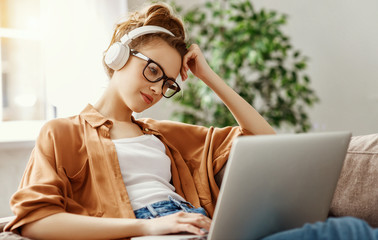 Intelligent and serious young woman in headphones using laptop on couch.