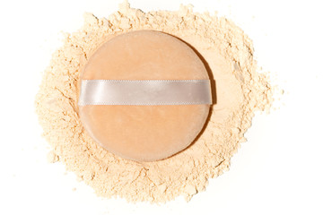 Scattered tan colored facial loose powder and puff on white background.