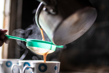 Tea being strained and poured into the cups from an aluminium tea pot in an Indian kitchen. Indian drink and beverages.