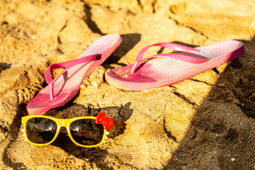 Warm summer. Sunglasses with a red bow are lying on the beach. There are rubber Slippers next to it.