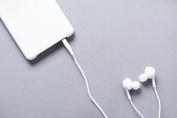Modern White earphones and mobile phone on a gray background. Minimalist style. Top view with copy space.