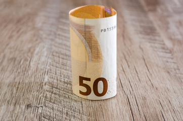 rolled up 50 euro banknote on a wooden background.