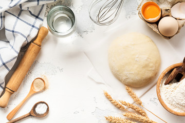 Dough and ingredients for the preparation of pasta, dough, eggs, flour, water and salt on a light rustic old table. Top view.