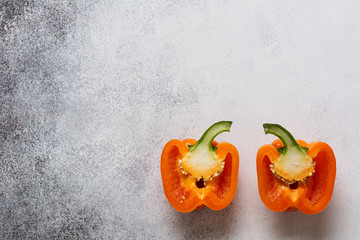 Two orange fresh peppers cut in half on a gray concrete old background. Cooking concept. Top view.
