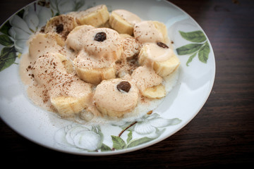 Banana fruit dessert with melted ice cream with chocolate, raisins and cinnamon and cocoa. Dark background.