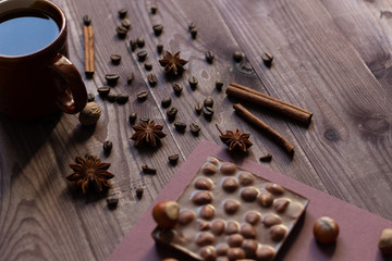 Chocolate bar with hazelnut, spice, cup of coffee on brown wooden background