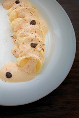 
Banana fruit dessert with melted creme brulee ice cream, raisins and cinnamon on a white plate. Dark background. insulation