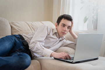 Young man lying on sofat and using laptop at home