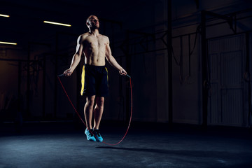 Fototapeta na wymiar Athletic young man training with skipping rope. Cardio workout with minimal equipment