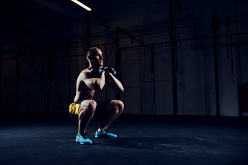 Fototapeta na wymiar Athletic man doing squats with kettlebells exercise at gym