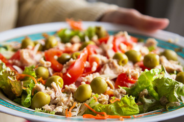 holding plate of salad with lettuce, tomato, onion and olives