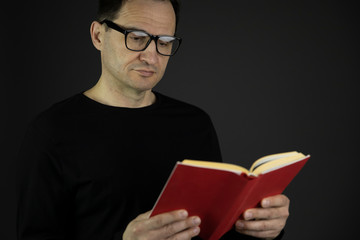 handsome casual dressed 40s man with dark hair in glasses closely reads red book isolated on black background copy space concept writer and his book. reading pleasure concept bookstore advertising