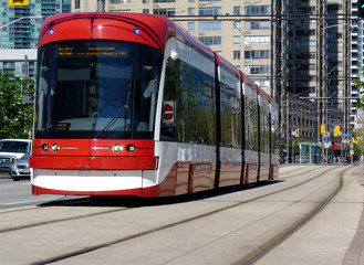 Fototapeta na wymiar Toronto Harbourfront streetscape and urban scene. concrete and glass condominium buildings background. red streetcar. low angle perspective. bright summer day, steel tracks and light car traffic.