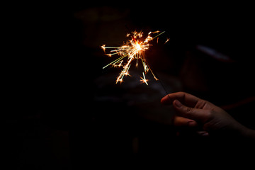 Female hand holding a burning sparkler, Christmas and new year sparkler holiday background