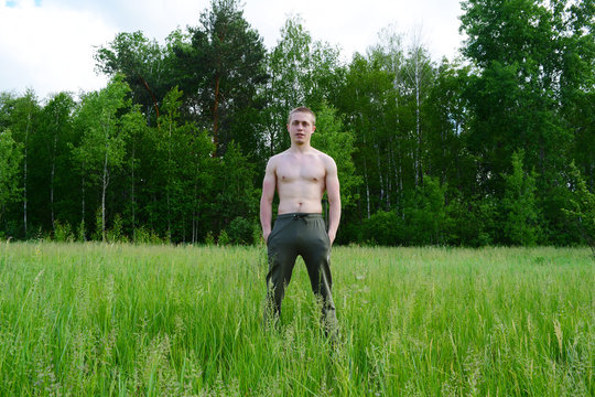 Young guy naked in trousers on nature green