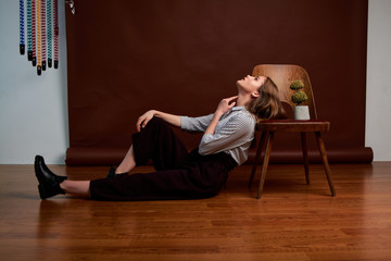 Gorgeous young female in classic suit, black shoes and grey coat. Vintage chair. Woman's clothes.