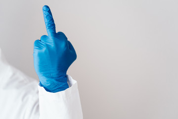 Fuck sign is showed by hand in a blue medical glove on a white background. Hand shows an obscene...