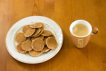 Bowl of mini stroopwafels and a cup of coffee on a wooden table. A stroopwafel is a traditional dutch cookie . Translation: koffie means coffee