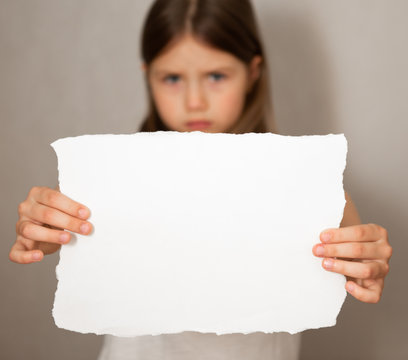 Conceptual image of a sad dejected little girl, holds a blank sheet of paper on gray background