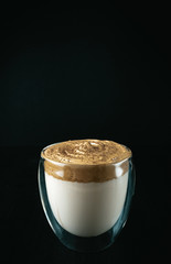 Dalgona coffee on a black background. Fashionable trendy drink made of milk and sweet whipped foam. Vertical photo
