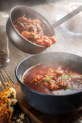 Borsch is poured into a bowl from a ladle from which steam, a traditional Ukrainian vegetable soup made from beets, carrots, tomatoes, potatoes, cabbage, herbs and garlic, close-up, shallow depth of