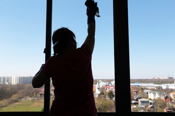 Window cleaning, silhouette of a woman washing the glass, inside view. Disinfection of home during...